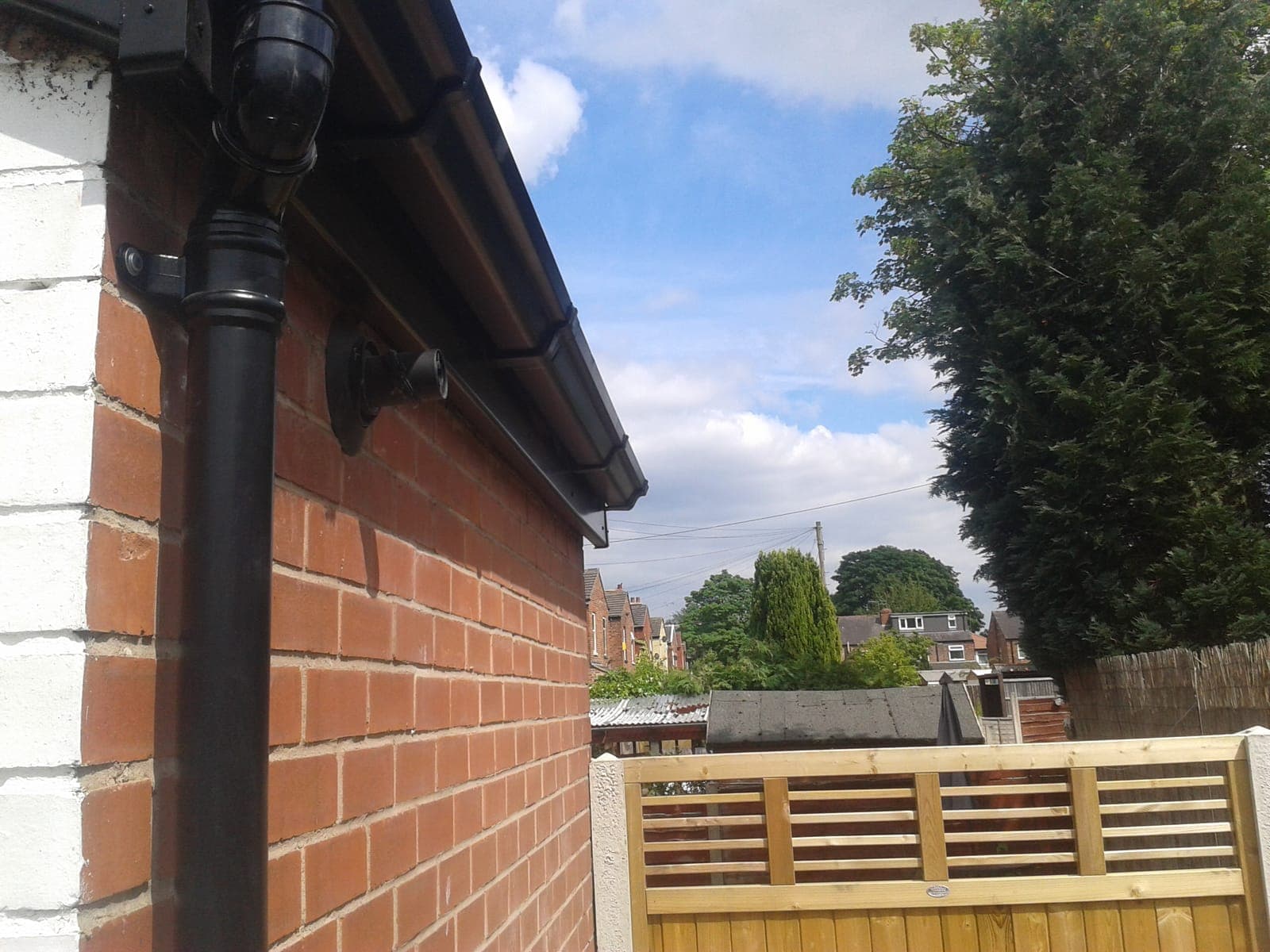 Neat black downpipe with a hopper and collar detail fitted against a brick wall