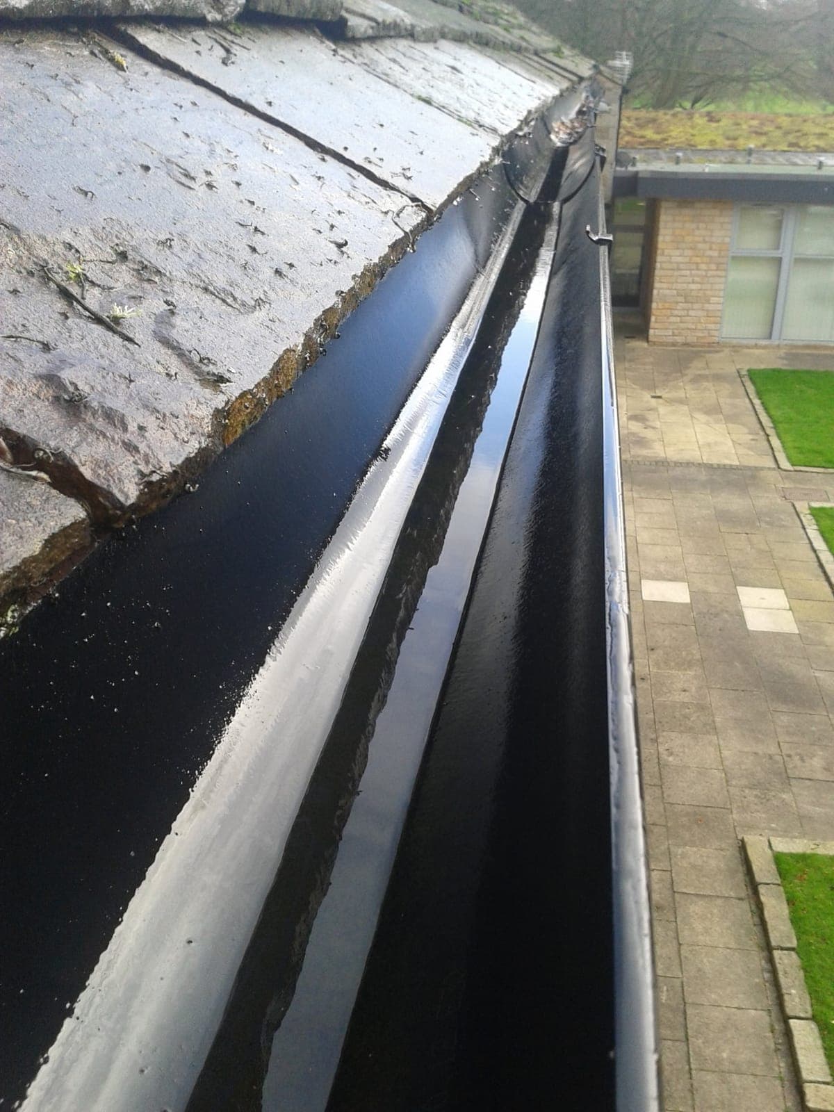 Clean, empty black gutter running along a slate roof after being cleared and flushed through