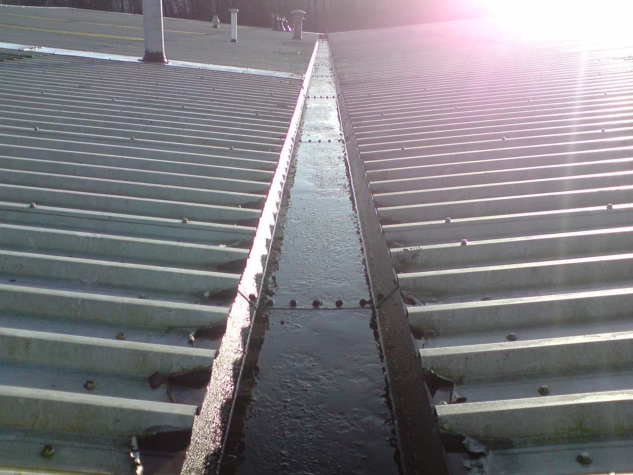 A cleared, black-lined industrial box gutter between two corrugated commercial roofs after cleaning