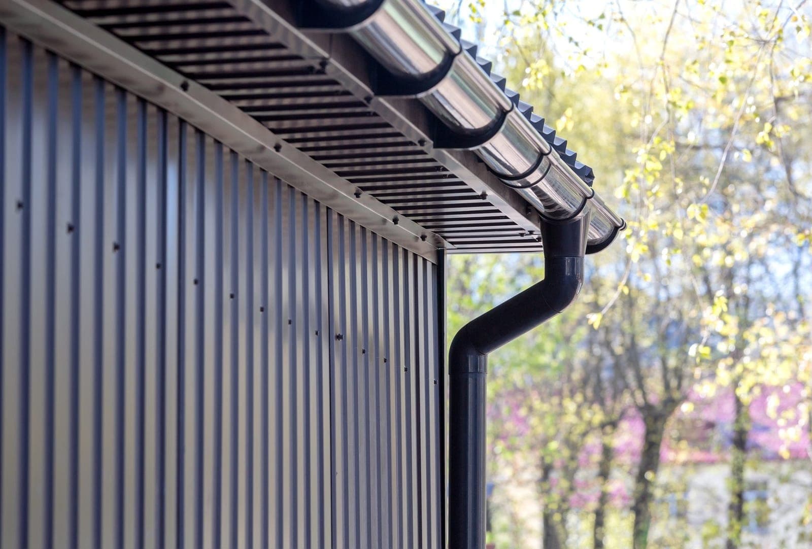 New black round guttering and downpipe fitted along the eaves of a house