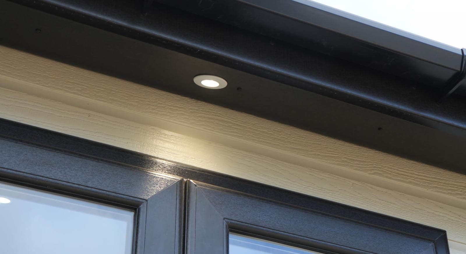 New black uPVC fascia and soffit with a recessed downlight and black guttering fitted above a window