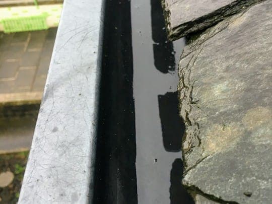 Clean, resealed black gutter sitting flush along the edge of a stone-slate roof